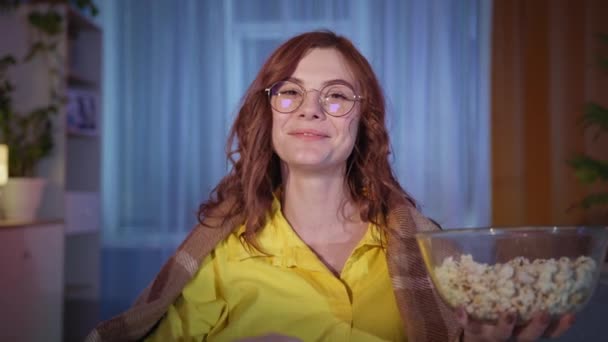 Fată adult cu ochelari mănâncă popcorn și se uită la un program amuzant în timpul timpului liber seara la domiciliu, stai acasă — Videoclip de stoc
