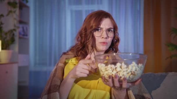 Γυναίκα τρώει ποπ κορν και παρακολουθεί προγράμματα ή ταινίες ενώ χαλαρώνει στο σπίτι το βράδυ — Αρχείο Βίντεο