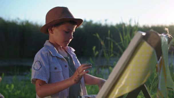 Creatieve kinderen, getalenteerde jongen tekent beeld met verf en handen op doek terwijl ze buiten rusten op het platteland in de buurt van rivier achtergrond van zonlicht — Stockvideo