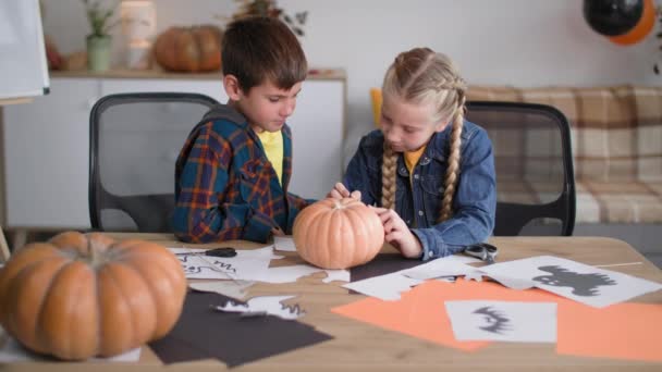 Halloween, los niños recortan imágenes para decorar la habitación y dibujan una cara de calabaza con una pluma de fieltro para celebrar las vacaciones de otoño — Vídeos de Stock