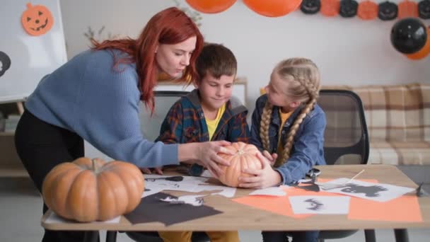 Lycklig familj, mamma med sina barn ritar en pumpa ansikte i dekorerat rum med bollar och ritningar, le och titta på kameran — Stockvideo