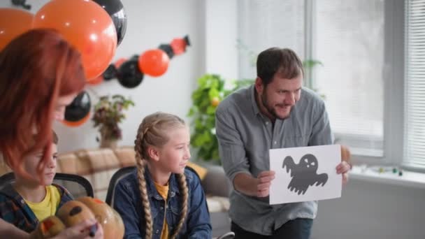 Halloween, rodina se baví přípravou dekorací na prázdninovou párty, radostný otec si hraje s dcerou a jizvení s kresbou duchů v útulném pokoji doma — Stock video