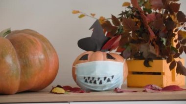 Cadılar bayramı salgını, güzel sonbahar dekoratif balkabağı tıbbi maskeli, ağızlıklı ve şapkalı parti odasındaki şifoniyerin üstünde duruyor.