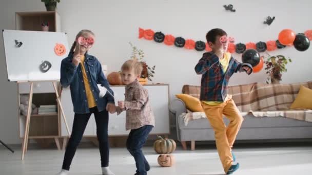 Halloween dance, funny male and female kids with decorative glasses pumpkins dancing in a festive cozy room — Vídeo de Stock