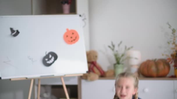 Podzimní prázdniny, vtipné mužské a ženské děti skákající ven a děsivé ukazující znamení boo v místnosti zdobené kresbami dýní a duchů, halloween — Stock video