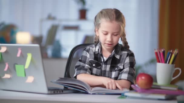 Female student of elementary grades doing homework reading book at home — Stockvideo