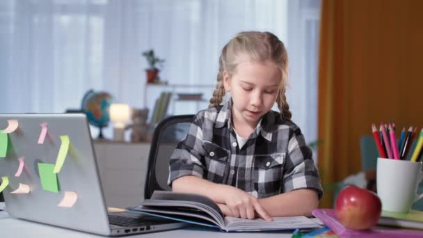 Children home schooled, little girl doing homework reading a book in room at table — Vídeo de Stock