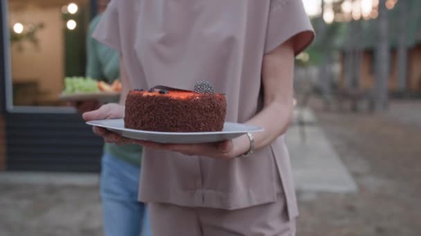 Festive dinner, young woman carries cake on platter and puts it on table during family dinner in garden — Stockvideo