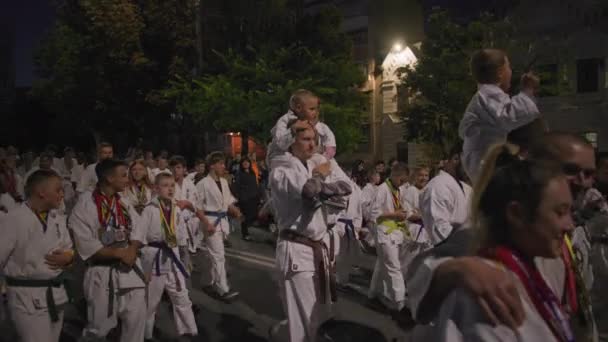 KHERSON, UKRAINE - 7 september 2021 Festival Melpomene van Tavria, menigte van karate kinderen in kimono marcheren tijdens feestelijke parade in de hoofdstraat in de stad in de late avond — Stockvideo