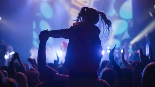 KHERSON, UKRAJNA-SZEPTEMBER 7, 2021: Tavriai Melpomén Fesztivál, lófarkas kislányok sziluettje, akik együtt ugrálnak apával a vállukon az éjszakai koncert alatt, az emberek tömegei tapsolnak — Stock videók