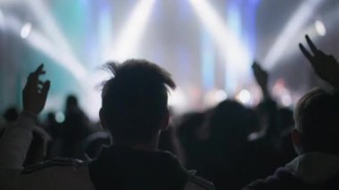 KHERSON, UKRAINE-SEPTEMBER 7, 2021: Tavria Melpomene Festivali, gençlerin arkadan baktığı kalabalık, açık havada aydınlatılmış bir konser sahnesinin arka planına kollarını kaldırarak atlayan insanlar