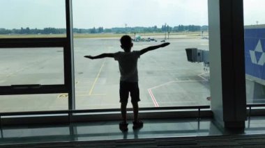 KIEV, UKRAINE-20 HAZİRAN 2021: Havalimanında pencere kenarındaki çocuk bir uçağın kanatları gibi kollarını açmış, havada uçan bir uçak gibi davranan küçük çocuk,