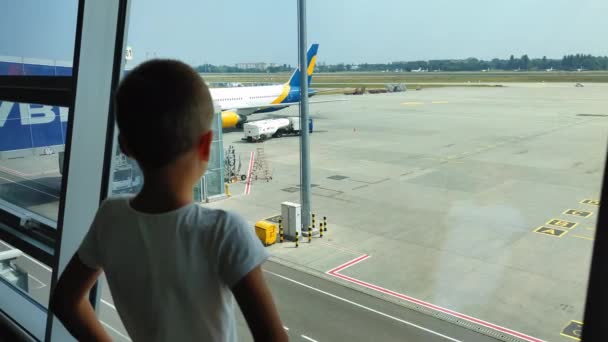 KIEV, UKRAINE-JULY 20, 2021: мандрівник, маленький пасажир біля великого вікна, дивиться на літак, потім обертається і посміхається в камері в аеропорту. — стокове відео