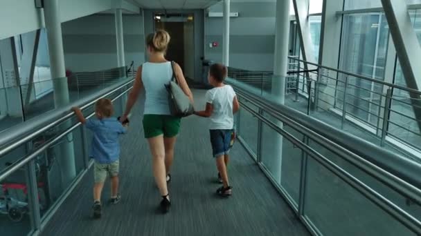 KIEV, UKRAJNA-JÚLIUS 20, 2021: családi nyaralás, anya fogja a kezét a gyerekek, és megy végig üvegfolyosón a repülőtér a repülés — Stock videók