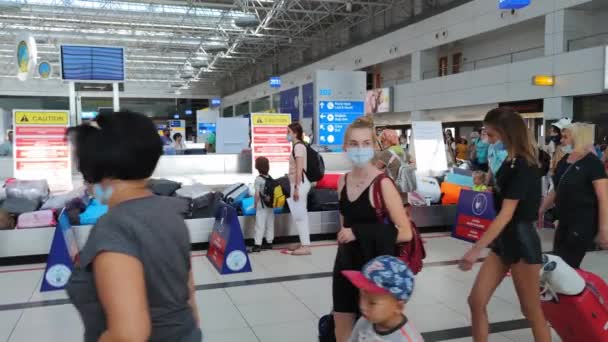 АНТАЛИЯ, ТУРЦИЯ - 21 июля 2021 года: аэропорт во время пандемии, туристы в масках забирают багаж с конвейера в зоне выдачи багажа — стоковое видео