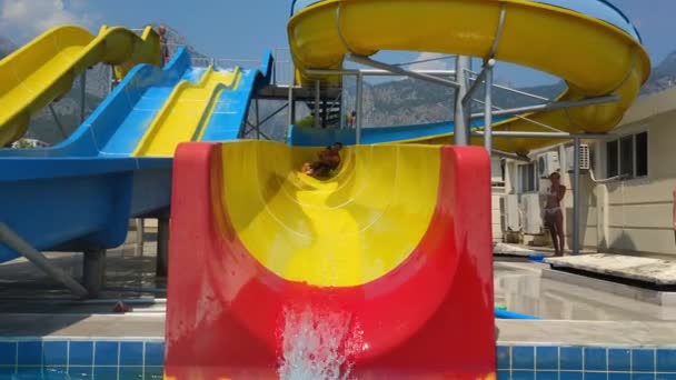 KEMER, TURQUÍA - 22 DE JULIO DE 2021: fin de semana familiar en el parque acuático, mamá activa e hijo pequeño con exceso de agua inflable bajan por el tobogán a la piscina — Vídeos de Stock