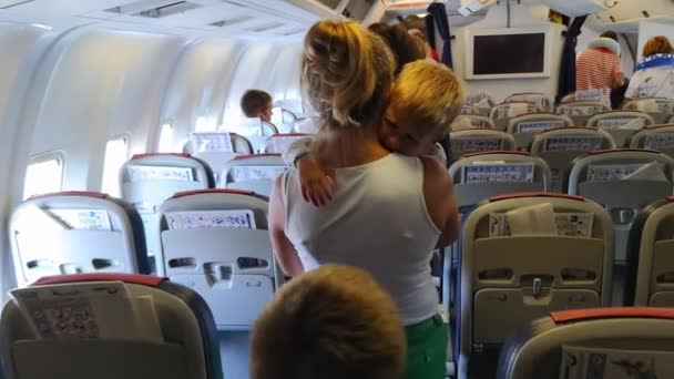 KIEV, UKRAINE - JULI 31, 2021: huilend kind in vliegtuig, moeder in medisch masker die het vliegtuig verlaat draagt een overstuur zoon die in slaap viel en de vlucht niet heeft gezien — Stockvideo