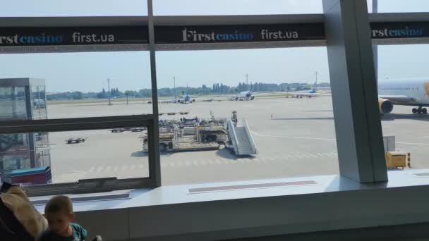 KIEV, UKRAINE - JULY 31, 2021: masked passengers pass through the glass corridor, airport during coronavirus pandemic, there are many planes in background — Stock Video