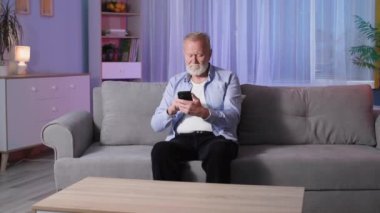 Yaşlılar için teknoloji, yeşil ekranlı cep telefonu tutan gri saçlı adam, modern büyükbaba koltukta otururken evde bir cihaz kullanıyor.