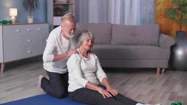 Šťastný aktivní důchodci doma, sportovní starší manžel pomáhá staré ženě s plným tělem protahování na podložku při tréninku — Stock video