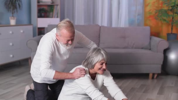 Elderly couple doing stretching on yoga mat at home, happy gray-haired husband and wife go in for sports and then look at camera together — 图库视频影像