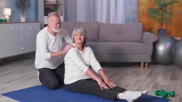 Активный здоровый образ жизни, пожилая женщина, делающая растяжку с помощью мужа, портрет счастливых спортивных пенсионеров — стоковое видео