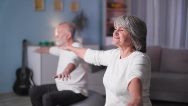 Deportes ancianos familia, feliz mujer y hombre haciendo entrenamiento de fitball en casa, pareja de jubilados con los brazos levantados gira a izquierda y derecha — Vídeo de stock