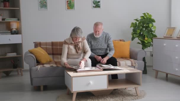 Ηλικιωμένη οικογένεια μαζί στον καναπέ με vintage φωτογραφικό άλμπουμ, παππούδες απολαμβάνοντας αναμνήσεις και συζητώντας ευχάριστες στιγμές με φωτογραφίες — Αρχείο Βίντεο