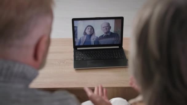 Gri saçlı evli çift yaşlı arkadaşlarıyla sohbet ediyor dizüstü bilgisayar kullanıyorlar, olgun erkek ve kadın evde kanepede otururken monitöre bakıyorlar. — Stok video