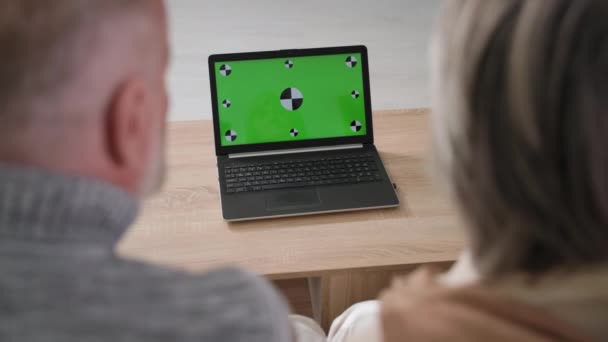 Senior homme et femme utilisent un ordinateur portable moderne avec écran vert à la maison, vue sur l'épaule, espace vide pour la mise en page — Video