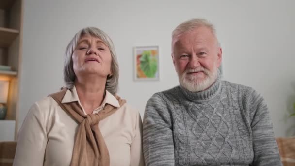 Счастливые пенсионеры машут руками веб-камере, портрет седовласых бабушки и дедушки общаются через Интернет дома — стоковое видео