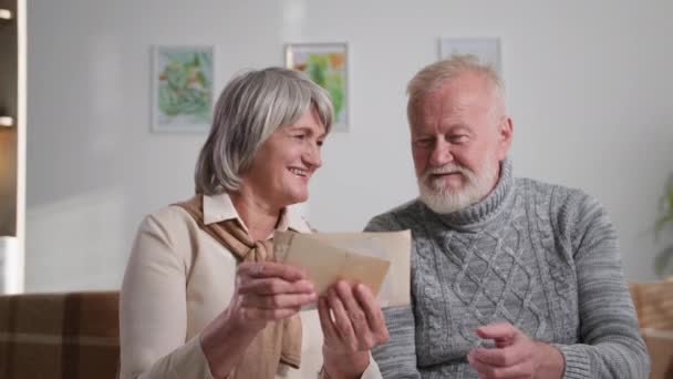 怀旧、快乐的老夫妇享受回忆，灰白头发的男人和女人在家里看有照片的旧相册 — 图库视频影像
