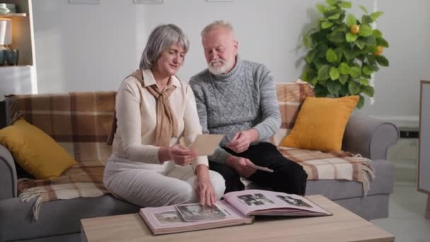 Ancianos de la vida y los recuerdos de la familia, canoso lindo envejecido pareja mirando las viejas fotos en el álbum en casa — Vídeos de Stock