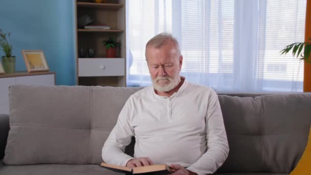 Ból pleców u starszych mężczyzn czytanie książki na kanapie, niezdrowy stary siwowłosy mężczyzna dotyka ból pleców — Wideo stockowe