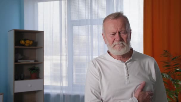 Chest pain, portrait of unhappy old man having heart attack at home, pensioner holding his chest with both hands — Stock Video