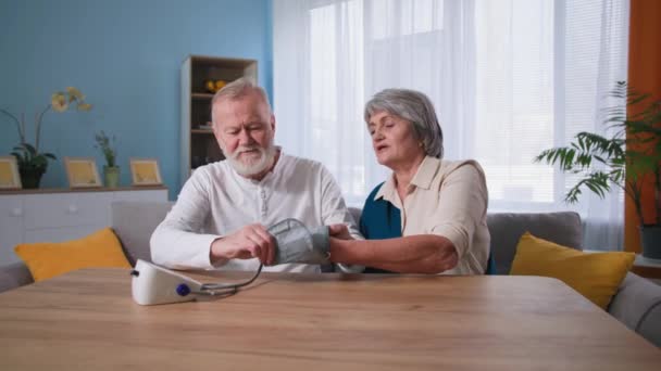 Medicinsk utrustning och hälso- och sjukvård, farfar använder digital mätning blodtryckskontroll för mormor vid bordet hemma — Stockvideo