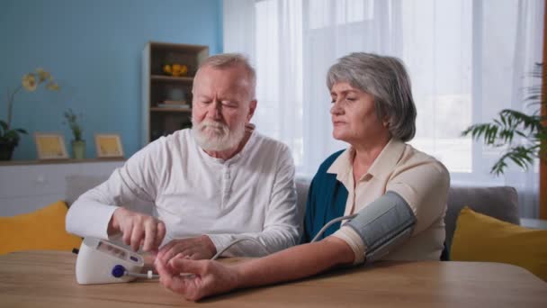 Kardiológia, idős pár vérnyomásmérés, idős férj és feleség magas vérnyomással — Stock videók