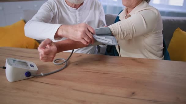 Meten van pols en bloeddruk voor migraine, oude man wordt op medische tonometer op zijn vrouw arm thuis — Stockvideo