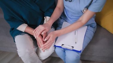 Yaşlılara destek olmak, kadın doktor üniforması giymek, evdeki tıbbi muayenede yaşlı büyükannenin elini tutmak, yakın görüş.
