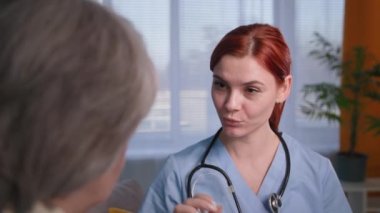 Steteskoplu genç bir kadın terapist yaşlı bir kadın hastayla koltukta oturuyor, nazik bir doktor yaşlı bir kadına danışıyor.