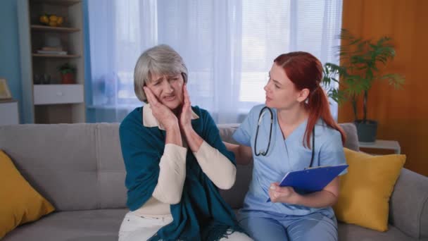 Patient âgé parle de douleurs dans sa tête au médecin traitant, médecin femme en uniforme bleu avec un stéthoscope soutient grand-mère à la maison — Video