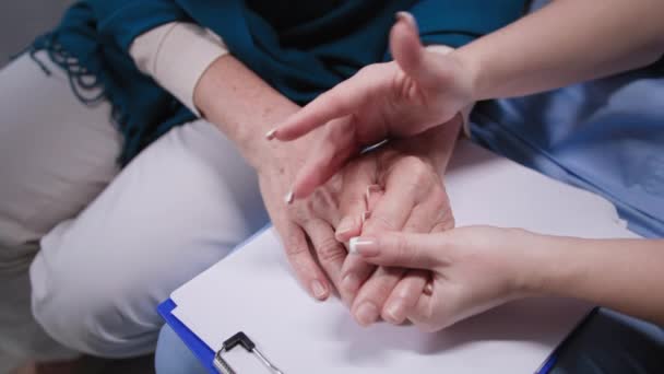 Assistenza agli anziani, giovane donna medico tiene le mani femminili anziane durante la visita medica a casa — Video Stock