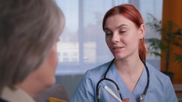 gyönyörű professzionális női terapeuta beszél idős beteg, háziorvos kék egyenruhában sztetoszkóppal jegyzetel konzultáció közben