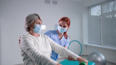 Emekliler spor ve sağlıklı yaşam tarzları için huzurevine gider, yaşlı kadınlar koltukta oturan fizyoterapistlere yardım ederek dambılları kaldırır.