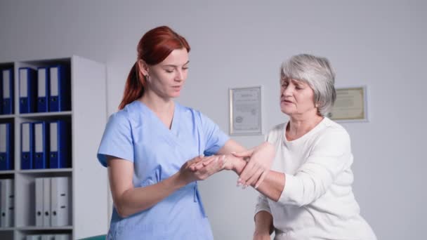 Vrouwelijke therapeut onderzoekt pijnlijke handen van een oudere grijze vrouw patiënt na een blessure close-up, fysiotherapie voor gepensioneerde — Stockvideo