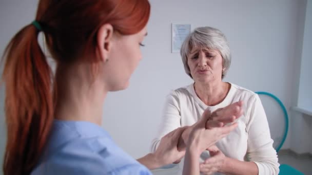 Idős nyugdíjas személy az orvosi vizsgálaton, ápolónő megvizsgálja a kezét ősz hajú idős nő sérülés után — Stock videók
