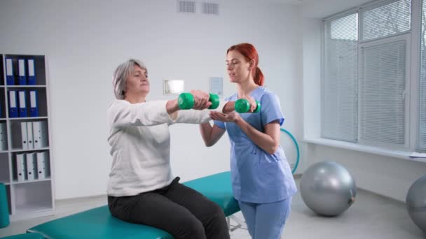 Lábadozás a sérülésből, fizioterapeuta egyenruhában dolgozik női beteggel a súlyzókkal való edzés alatt — Stock videók
