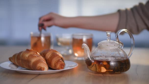 Ochtendrituelen, kruidenthee in theepot met croissant op bord, jonge vrouw giet suiker in beker met warme drank zitten in de ochtend aan tafel tijdens het ontbijt — Stockvideo