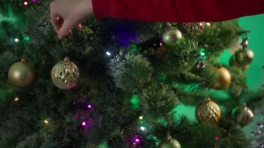 preparation for winter holiday, unrecognizable young woman hangs balls on a Christmas tree close-up, toys and flashing garland on artificial branches