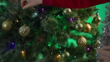new year during quarantine, unrecognizable girl hangs balls and a protective medical mask on Christmas tree with flashing garland on xmas Eve